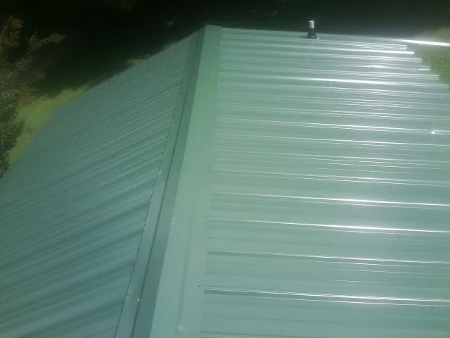 New green metal panels meeting at the ridge of a roof — Flat Roof Repair work by our crew in Keene